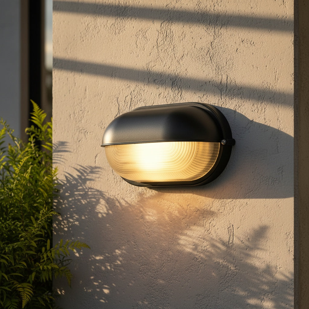 black aluminum Acolyte wall lamp illuminating brick entryway at dusk