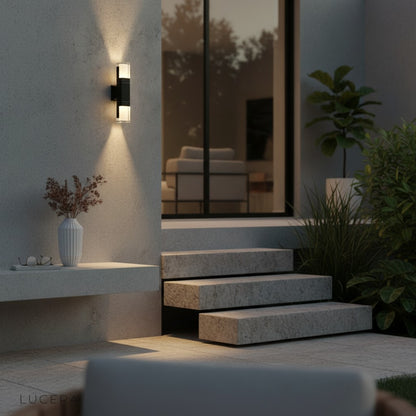 Merle LED wall light casting soft glow beside a wooden entry door at dusk