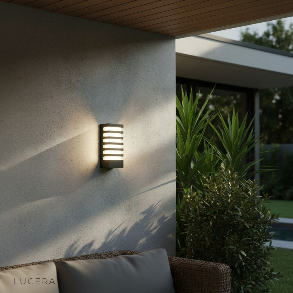 warm glow from Quinn sconce casting light on textured stone garden wall at night