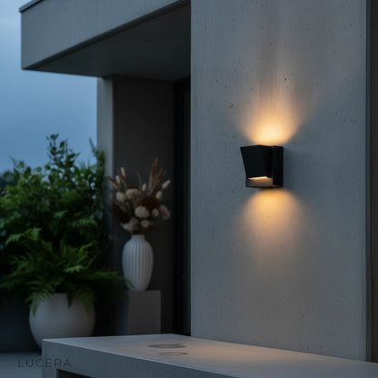 Cora LED sconce above an outdoor dining table with soft ambient evening lighting