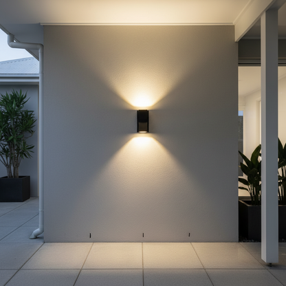 Cora outdoor light mounted on a stucco wall near a potted olive tree, warm glow