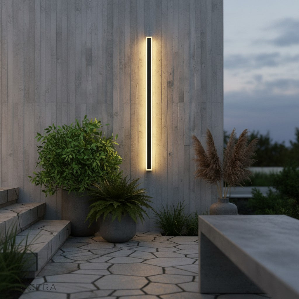 outdoor living room with Odette wall lamp beside lounge chairs and greenery at twilight