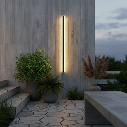 outdoor living room with Odette wall lamp beside lounge chairs and greenery at twilight