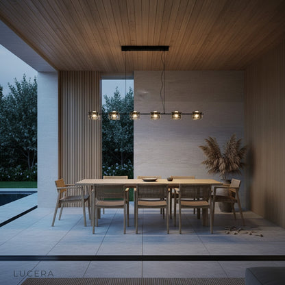 Copper and glass chandelier suspended over a rustic wooden dining table in evening light