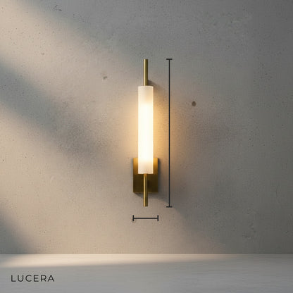 front view of modern gold wall sconce with vertical glass shade mounted on neutral wall in clean studio setting