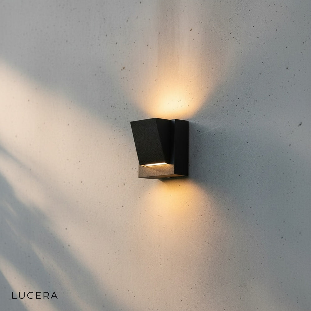 Cora outdoor wall light in warm glow beside a wooden entry door with stone cladding