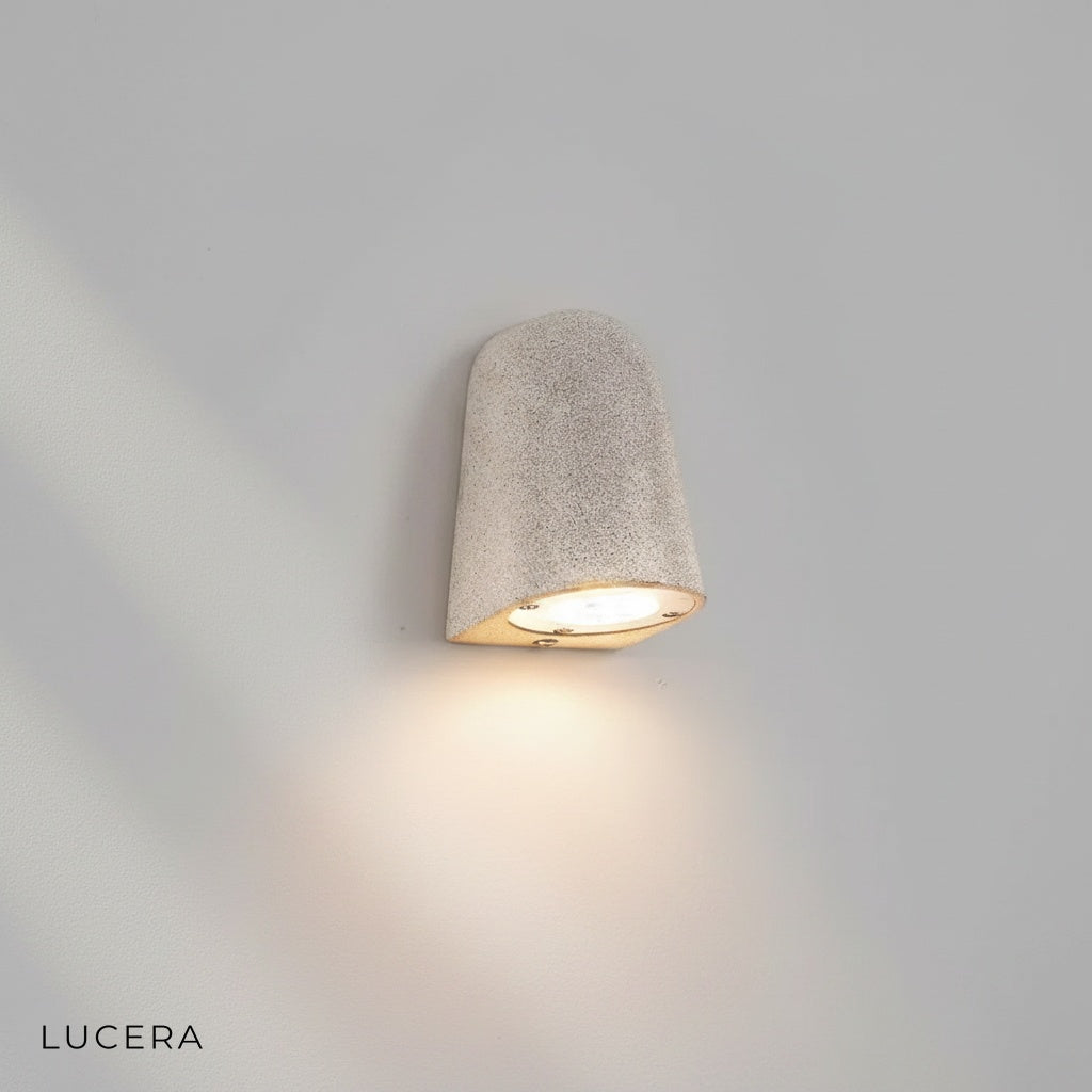 Side angle studio view of Lucera Eos wall light showing textured microcement and aluminum frame