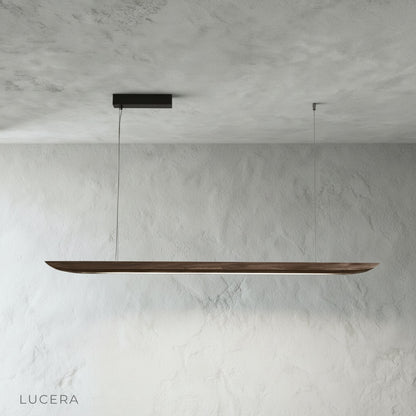 Front view of the Fauvist pendant light with natural wood grain and warm diffused glow in a bright studio setting