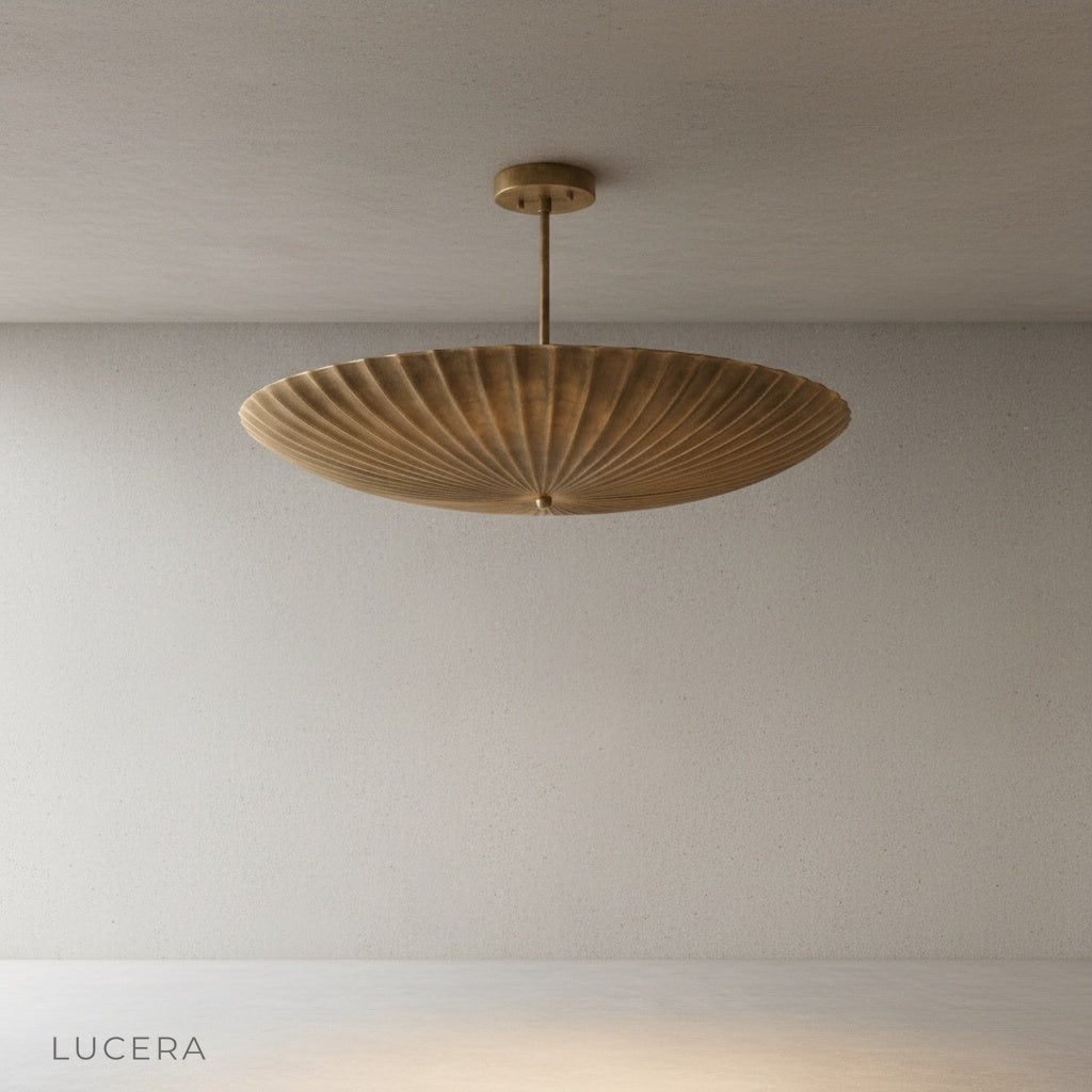 Side angle studio view of the sculptural brass pendant light showing wide fluted shade and cord