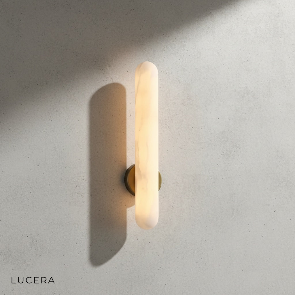 Cosmo Alabaster sconce illuminated in a dim hallway casting soft ambient light on textured plaster walls