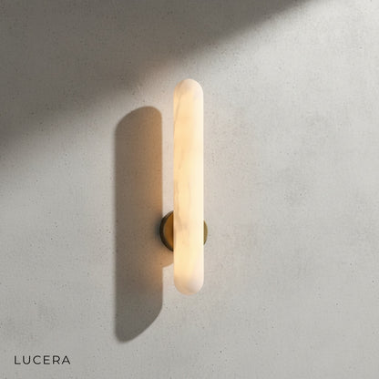Cosmo Alabaster sconce illuminated in a dim hallway casting soft ambient light on textured plaster walls
