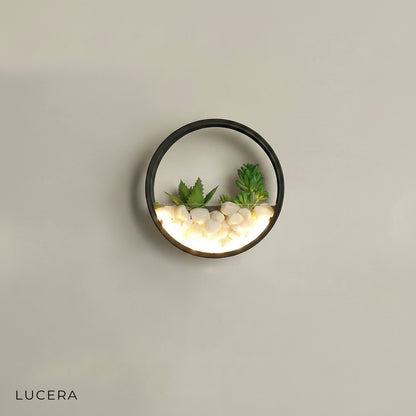 Close-up of Laine wall lamp warm LED glow through acrylic and plant accents