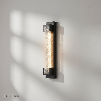 black outdoor sconce with warm LED light casting elegant shadows on garden wall