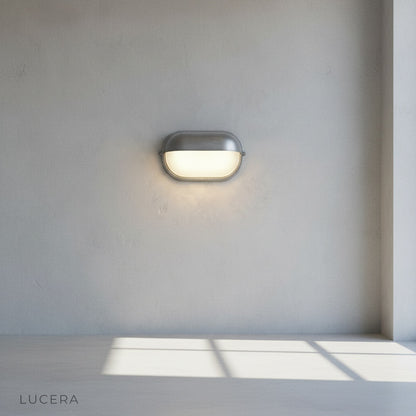 Acolyte wall lamp with warm LED glow against dark wood exterior wall