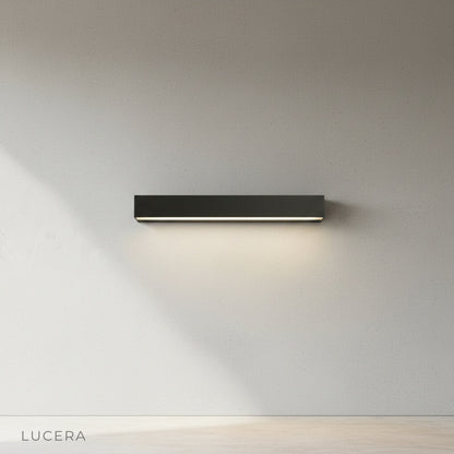 Goccia wall lamp in matte black finish mounted on brick wall, daytime natural light