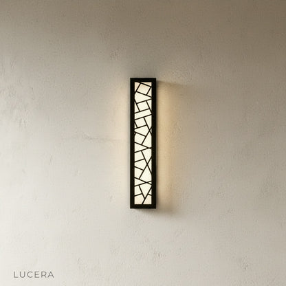 Emblem Wall Lamp casting warm light on a textured stone wall outdoors