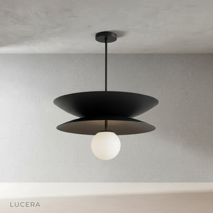Tremulous pendant light in polished brass finish suspended in minimalist studio setting