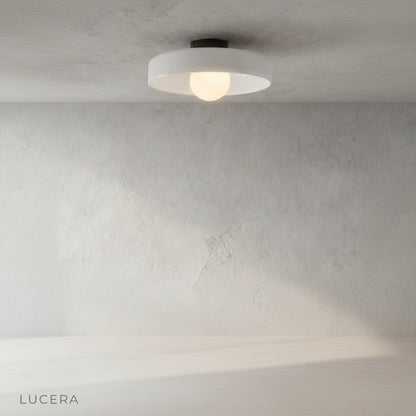 Madder ceiling light as wall sconce in a cozy reading nook, colored glass body glowing against neutral wall