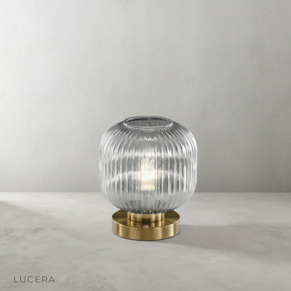 ribbed glass table lamp with brass accents on dark oak shelf in study
