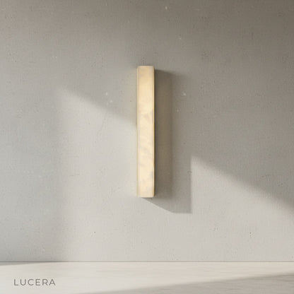 Brass and alabaster wall light illuminating dark brown wall in contemporary entryway