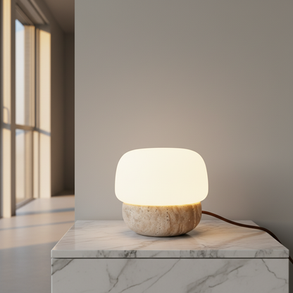 Jut Table Lamp on travertine base glowing warmly on a modern bedroom nightstand