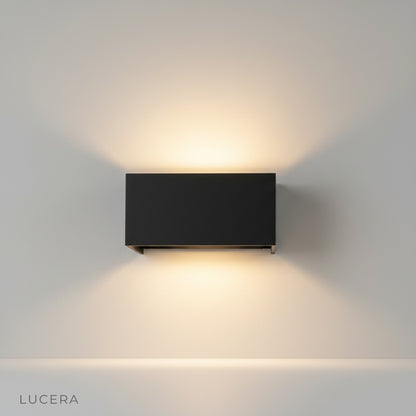 modern black dowel outdoor wall lamp illuminating brick patio wall at dusk