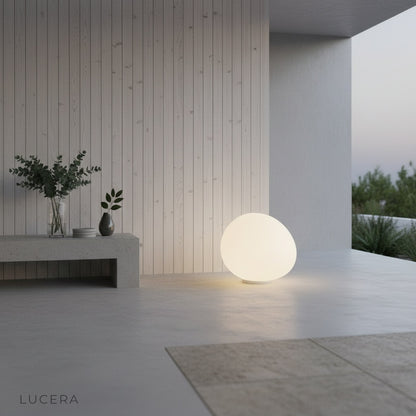 Yttrium Outdoor Floor Lamp illuminated on a stone terrace with greenery and string lights in background