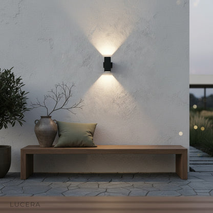 sleek outdoor sconce lighting up a modern entryway with stone cladding and plants